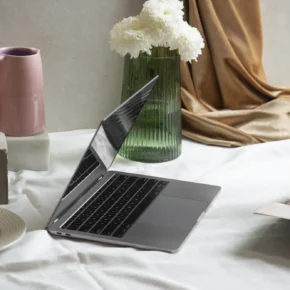 Öppen laptop på ett bord med vas och blommor i mjukt naturligt ljus.